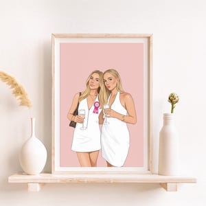 Peut inclure: Illustration encadrée de deux femmes en robes blanches, tenant des flûtes de champagne. L'une porte un ruban rose. Le fond est rose clair. L'œuvre est exposée sur une étagère avec des vases décoratifs.