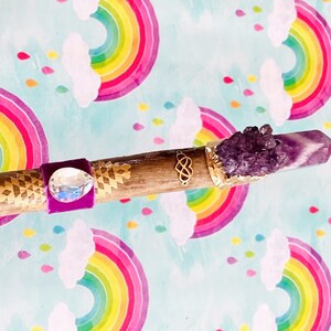 Puede incluir: Una varita de madera con detalles de terciopelo morado y dorado, adornada con cristales transparentes y un gran cristal de amatista en la parte superior.