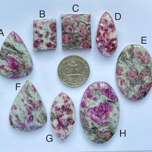 May include: Eight cabochon gemstones in a variety of shapes and sizes. The stones are a mix of green, white, and pink with a speckled pattern. A US quarter is included for scale.