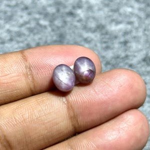 以下が含まれることがあります： 虹色の光沢のある仕上げを施した、2つの楕円形の紫色のスターサファイア