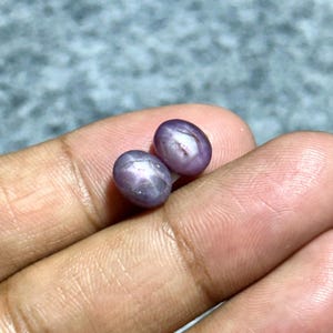 Könnte beinhalten: Zwei ovale, sternförmige Rubine in violetter Farbe mit einem sechszackigen Stern in der Mitte.