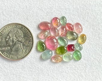 May include: A collection of 18 oval and teardrop shaped gemstones in various shades of pink, green, and blue. The gemstones are arranged on a white surface.