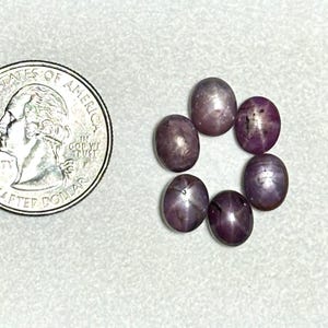 May include: Seven round, purple star sapphires, each with a six-pointed star in the center, arranged in a circle around a quarter.