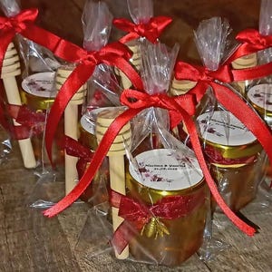 Peut inclure: Petits pots en verre remplis de miel, chacun avec un couvercle doré et un bâtonnet à miel en bois. Les pots sont enveloppés dans du cellophane transparent et attachés avec un ruban de satin rouge. Une breloque dorée en forme d'abeille orne le devant de chaque pot.