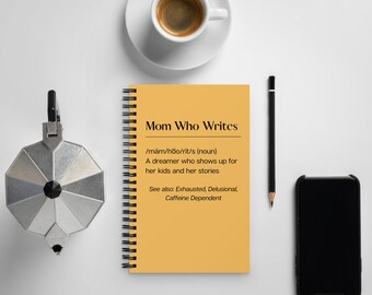 May include: A yellow notebook with a spiral binding. The notebook has the text "Mom Who Writes" on the cover. The text below the title reads "/mäm/hoo/rit/s (noun) A dreamer who shows up for her kids and her stories See also: Exhausted, Delusional, Caffeine Dependent".