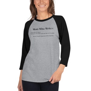 May include: A gray and black baseball tee shirt with the text "Mom Who Writes" and a definition of the term. The definition reads: "(noun) A dreamer who shows up for her kids and her stories. See also: Exhausted, Occasional Caffeine Dependent."