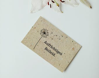 May include: A card with a dandelion graphic and the text "Aufrichtiges Beileid." The card is made of recycled paper and has a natural brown color.