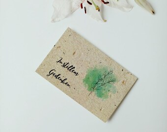 May include: A card with a watercolor background and a green branch with leaves. The text on the card reads "In stillem Gedenken."
