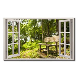 May include: A wooden bench sits in a clearing in a forest, viewed through an open window. The window is white with a white frame. The bench is made of rough-hewn wood and has a rustic look. The forest is lush and green, with trees in the background.