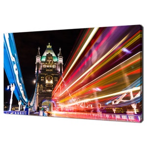 May include: A night view of Tower Bridge in London, England. The bridge is lit up with colorful lights, and there are streaks of light from cars driving across the bridge. The bridge is a popular tourist destination and a symbol of London.