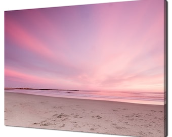 May include: A pink and purple sunset over a sandy beach with a calm ocean in the distance.