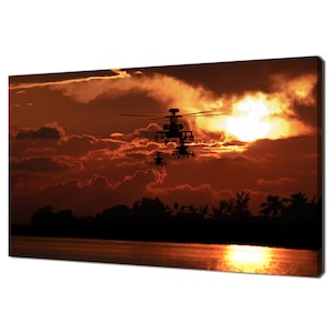 May include: Silhouettes of three military helicopters flying in formation against a fiery orange sunset sky. The helicopters are flying low over a body of water with a line of trees in the background.
