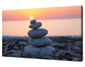 Puede incluir: Una pila de piedras grises equilibradas una encima de la otra en una playa al atardecer. El sol se pone sobre el océano en el fondo.