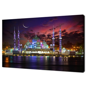 May include: A mosque with a crescent moon in the sky at night. The mosque is lit up in purple, blue, and white lights. The mosque is reflected in the water.
