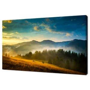May include: A panoramic view of a misty mountain landscape at sunrise. The sun shines through the fog, illuminating the green trees and golden grass in the foreground. The sky is a vibrant blue with wispy clouds.
