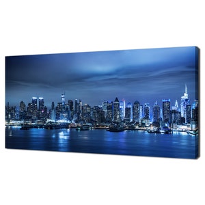 Könnte beinhalten: Ein Panoramablick auf eine Skyline einer Stadt bei Nacht. Die Stadt ist mit hellen Lichtern beleuchtet, und die Gebäude spiegeln sich im Wasser. Der Himmel ist tiefblau, und in der Ferne sind Wolken zu sehen.