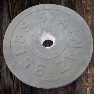 Puede incluir: Una placa de peso de hierro fundido gris con el texto "2.5 LBS" y "STAIN" en ella.