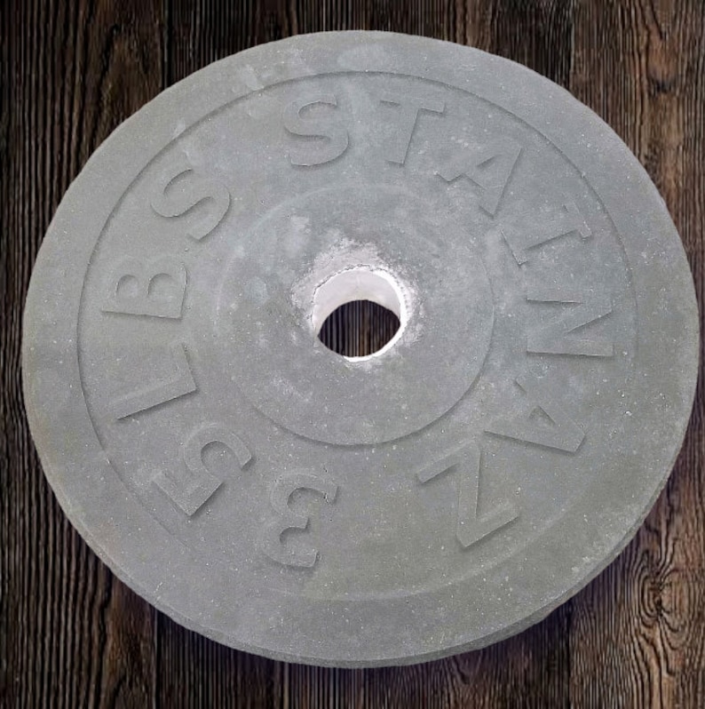Puede incluir: Una placa de peso de hierro fundido gris con el texto "2.5 LBS" y "STAIN" en ella.