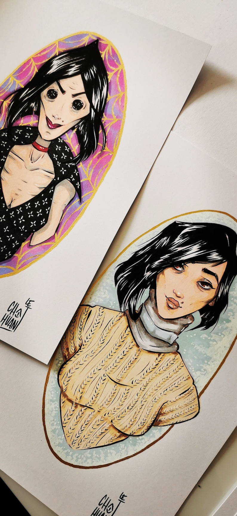 May include: Two watercolor illustrations of women with black hair. The first woman is wearing a black and white patterned top with a red choker. She is surrounded by a pink and gold oval with a spiderweb design. The second woman is wearing a yellow sweater and a white turtleneck. She is surrounded by a blue and gold oval.