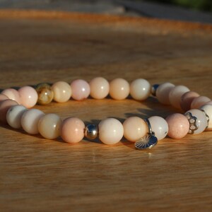 Peut inclure: Un bracelet en perles roses et blanches avec un charme argenté. Le bracelet est fait de pierres naturelles et a un look délicat et féminin.