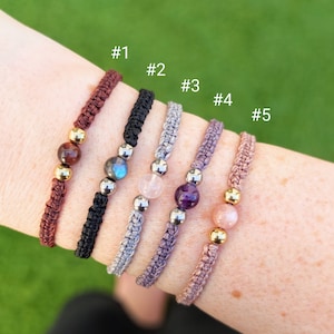 Peut inclure: Cinq bracelets avec des cordons de couleurs différentes et des perles de pierres précieuses. Les bracelets sont numérotés de 1 à 5. Les perles sont rouge foncé, bleu-vert, rose clair, violet et rose clair.