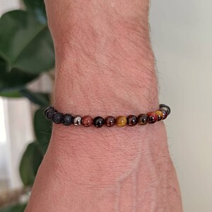 Peut inclure: Un bracelet en perles avec des perles de lave noire, de œil de tigre et de jaspe rouge.