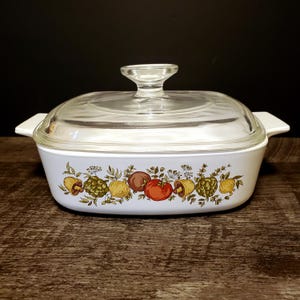 May include: White rectangular casserole dish with a clear glass lid. The dish has a colourful border of various vegetables, including tomatoes, artichokes, and onions. The handles are white.