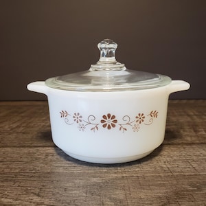 May include: White casserole dish with a glass lid and a brown floral design. The dish has two handles on the sides.