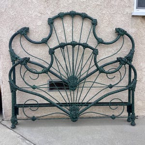 Könnte beinhalten: Ein antiker, dunkelgrüner Metallbettrahmen. Das Kopfteil weist ein verziertes, fächerförmiges Design mit floralen Verzierungen auf. Der Rahmen hat eine Used-Optik, die seinen Vintage-Charme unterstreicht. Für eine Matratze in Standardgröße konzipiert.