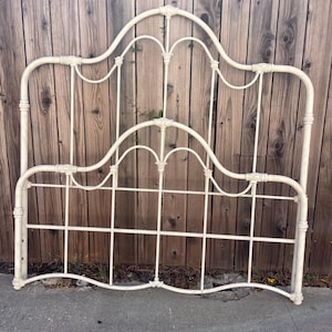 May include: An off-white metal headboard featuring a curved top rail with decorative finials and a grid-like structure. The frame is constructed from tubular metal with vertical and horizontal bars, showcasing a symmetrical design with arched elements.