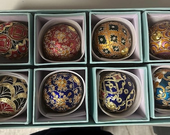 May include: A set of eight spherical ornaments arranged in a light blue box. Each ornament features intricate, colorful patterns with gold-toned filigree details, including floral, geometric, and swirling motifs in shades of red, blue, gold, and black.