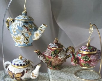 Puede incluir: Cuatro tetera de porcelana en miniatura con intrincados diseños florales y detalles dorados. Las teteras se exhiben en un soporte de metal y son perfectas para una fiesta de té o como adornos decorativos.