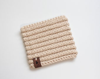 May include: A beige crocheted coaster with a brown leather tag. The tag has a small heart design.