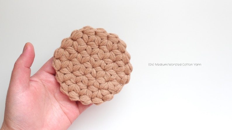 May include: A round, tan-colored crochet coaster featuring a textured puff stitch pattern. The item is labeled with the text (04) Medium/Worsted Cotton Yarn, indicating the material used to create this circular, hand-stitched textile piece.