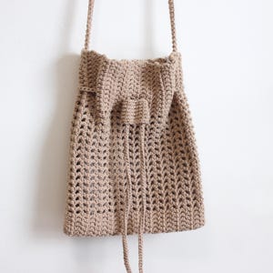 May include: A brown crocheted drawstring bag with a long strap. The bag has a  pattern of small holes throughout.