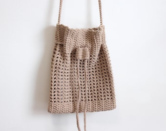 Puede incluir: Una bolsa de cordón de crochet marrón con una correa larga. La bolsa tiene un patrón de pequeños agujeros en todo.
