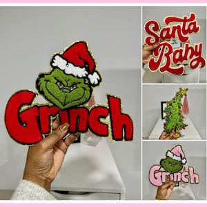 Op de afbeelding: Een collage van kerstversieringen. Eén toont de Grinch met een kerstmuts en het woord "Grinch" in het rood. Een andere zegt "Santa Baby" in rood script. Een derde zegt "Santa Baby" in roze met gouden rand.
