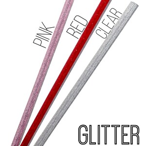 K&ouml;nnte beinhalten: Drei Glitzer-Trinkhalme in Pink, Rot und Klar. Die Strohhalme liegen auf einer wei&szlig;en Oberfl&auml;che. Der Text "PINK", "RED" und "CLEAR" steht &uuml;ber jedem Strohhalm. Der Text "GLITTER STRAWS" steht unter den Strohhalmen.