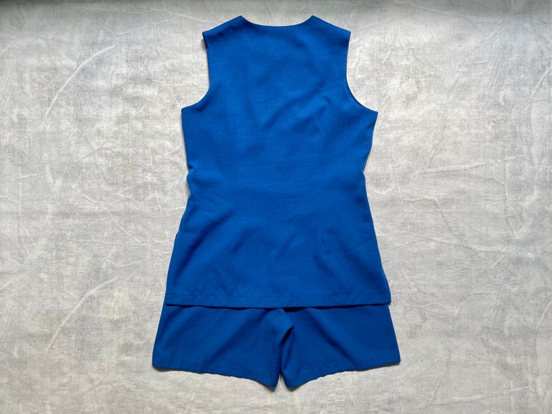 Op de afbeelding: Een blauwe, mouwloze jurk met een bijpassend short. De jurk heeft een simpel ontwerp en een licht uitlopende rok.
