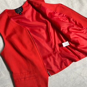 May include: A red sleeveless waistcoat with a zip fastening. The waistcoat has a lining and a label that reads "Alixandra" with the size "S" on it.