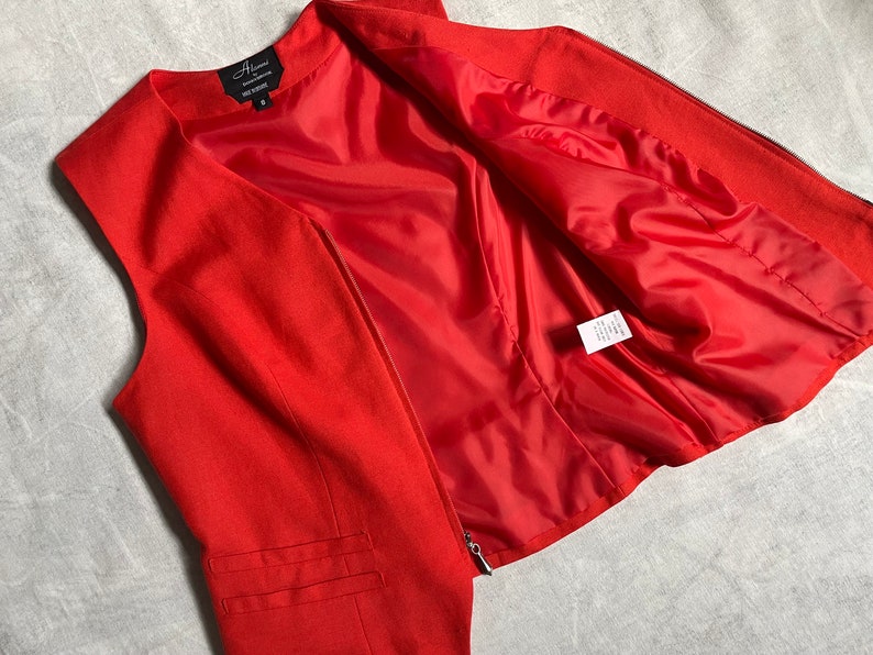May include: A red sleeveless waistcoat with a zip fastening. The waistcoat has a lining and a label that reads "Alixandra" with the size "S" on it.