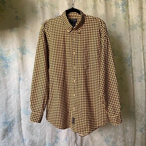 May include: A long-sleeved button-down shirt with a yellow and brown polka dot pattern. The shirt is hanging on a black hanger. The shirt has a button-down collar and buttoned cuffs.
