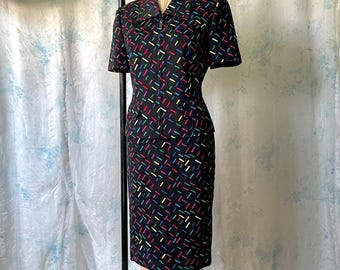 May include: A vintage black skirt suit with a colorful geometric pattern. The short-sleeved jacket has a notched collar and a zipper closure. The pencil skirt is knee-length. The suit is displayed on a mannequin.