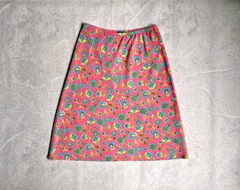 May include: A pink skirt with a floral pattern. The skirt features a repeating design of blue and green flowers and leaves on a pink background. The skirt has an elastic waistband.