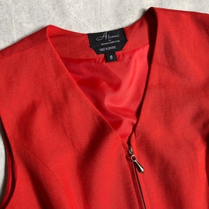 May include: A red sleeveless dress with a zip fastening and a v-neck. The dress has a label that reads "Alanni by Donnbrooke Made in Brisbane 8".