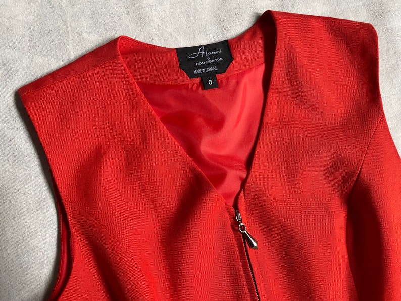 May include: A red sleeveless dress with a zip fastening and a v-neck. The dress has a label that reads "Alanni by Donnbrooke Made in Brisbane 8".