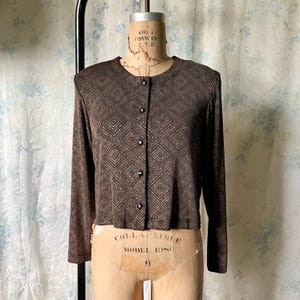 May include: A brown long-sleeved button-up shirt with a geometric pattern. The shirt has a round neckline and is made of a shiny fabric.
