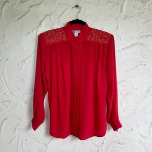 May include: A red long-sleeved blouse with a button-up front and gold and blue embellishments on the shoulders.