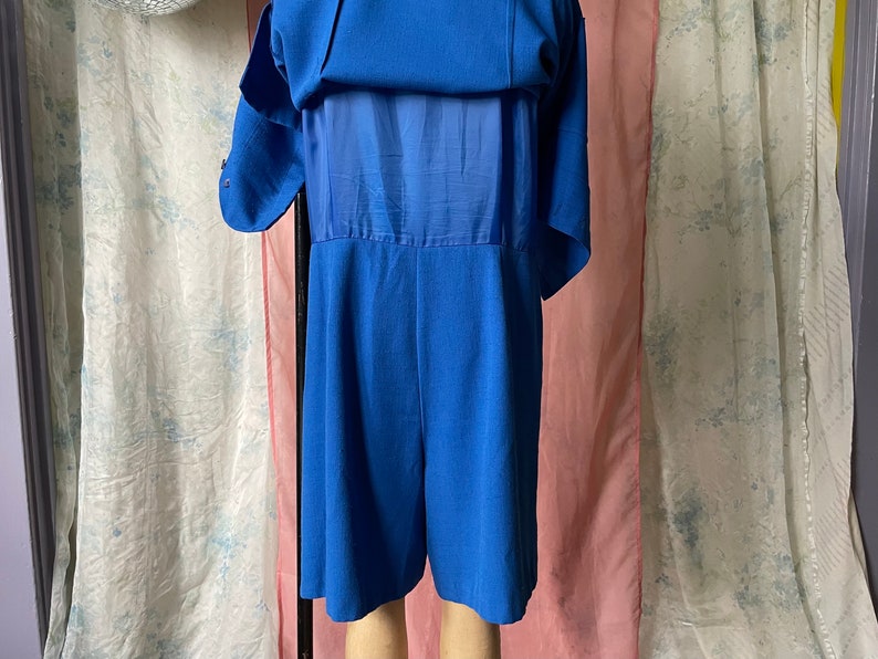 Op de afbeelding: Een koninklijk blauwe jumpsuit met korte mouwen en een transparante overlay op de rug.