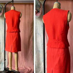 May include: A sleeveless red dress with a matching waistcoat. The dress has a fitted bodice and a skirt that falls to the knee. The waistcoat has a pointed collar and a button closure.